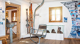 Ein historischer Skilift hat seinen Platz in einem Museum. Im Hintergrund sind historische Skiausrüstungen und Fotos ausgestellt.