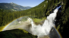 Ein beeindruckender Wasserfall stürzt in ein grünes Tal. Ein Regenbogen erscheint im Sprühnebel des Wassers.