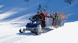 Eine motorschlittenfahrt führt durch den Schnee. Eine Gruppe von Menschen sitzt auf einem Schlitten, der hinter dem Fahrzeug gezogen wird.
