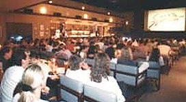 Film-Szene Ottensheim in Ottensheim: Eine große Menschenmenge in einem Innenraum. Es scheint sich um ein Restaurant oder eine Gaststätte zu handeln, mit Tischen, Stühlen und Gästen an den Tischen. Die Beleuchtung ist gedämpft, aber ausreichend, um den Raum und die Gäste deutlich zu erkennen.