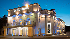 Ein elegantes Theatergebäude mit einer hell erleuchteten Fassade. Es ist Abend und der Himmel ist klar.