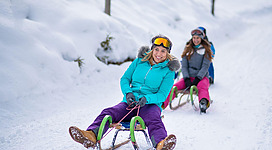 Fröhliche Erwachsene beim Rodeln auf verschneiter Piste in Altenmarkt-Zauchensee