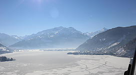 Zwei Personen skaten auf einem gefrorenen See. Die umliegende Berglandschaft ist wunderschön und sonnig.