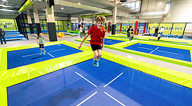 Ein Trampolinpark mit bunten Trampolinen in hellgrüner und blauer Farbe. Mehrere Jugendliche hüpfen und haben Spaß in der Einrichtung.
