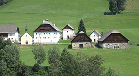 Ein malerisches Dorf in einer grünen Landschaft mit traditionellen Häusern. Die Umgebung ist friedlich und von Bäumen umgeben.