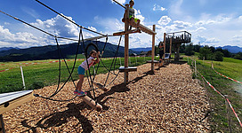 Ein Spielplatz im Freien mit Klettergerüsten und Schaukeln. Kinder spielen und genießen die schöne Landschaft bei sonnigem Wetter.