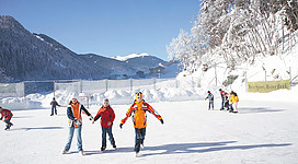 Kinder die an einem sonnigen Tag auf dem Eislaufplatz in Viehhofen Schlittschuh laufen.