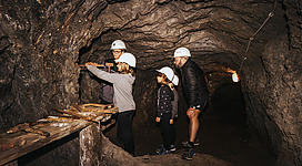 Eine Gruppe von Menschen erkundet einen unterirdischen Tunnel mit professionellen Helmen. Sie untersuchen die Wände und sind an der Geschichte des Ortes interessiert.