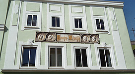 Stammhaus der Schwanthaler in Ried im Innkreis: Ein mehrstöckiges Gebäude mit hellen Fensterrahmen und klassischer Fassadengestaltung. Dekorative Elemente und Verzierungen schmücken die Außenwand, was dem Gebäude einen traditionellen, historischen Charakter verleiht.