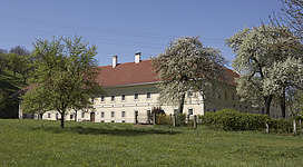 Sumerauerhof St. Florian in St. Florian: Ein mehrstöckiges Gebäude mit traditioneller Architektur, umgeben von blühenden Bäumen und Sträuchern auf einer grünen Wiese. Das Gebäude hat ein Satteldach und mehrere Schornsteine. Die Fassade ist hell und wirkt gepflegt. Vor dem Gebäude ist eine Grünfläche zu sehen, auf der vereinzelt Bänke oder andere Sitzmöglichkeiten stehen könnten.