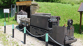 Barbara-Schaustollen in Wolfsegg am Hausruck: Eine Sammlung unterschiedlicher Ausrüstungsgegenstände und Fahrzeuge, die offenbar für militärische Zwecke genutzt werden. Die Objekte befinden sich auf einem Schotterplatz, umgeben von grüner Vegetation.