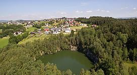 Naturbad Resilacke (Felsenbad) in Kleinzell im Mühlkreis: Auf dem Bild sieht man eine idyllische Landschaft mit einem Bergdorf. Inmitten grüner Hügel und Wälder liegt ein See. Die Häuser des Ortes sind überwiegend mit roten Dächern ausgestattet und in eine hügelige Umgebung eingebettet. Die Szenerie vermittelt einen friedlichen und malerischen Eindruck.