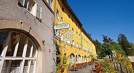 Ein charmantes, gelbes Gebäude mit einem einladenden Außenbereich. Es gibt viele Tische und Stühle im Freien, ideal für eine entspannte Zeit.