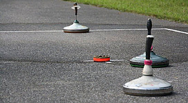 Asphaltstockbahn in St. Aegidi: Auf der Straße befinden sich mehrere runde Objekte in unterschiedlichen Farben, die möglicherweise für einen Wettbewerb oder eine Aktivität verwendet werden. Die Objekte sind auf einer Asphaltfläche platziert, die von einer grünen Wiese umgeben ist.