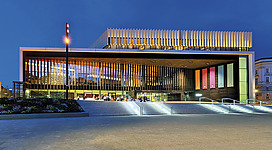 Musiktheater am Volksgarten, Linz: Modernes Theatergebäude mit beleuchteter Fassade und vertikalen Lamellen in der Abenddämmerung.