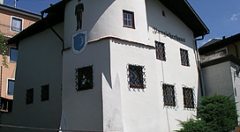 Zinngießerhaus in Mattighofen: Ein mehrstöckiges Gebäude mit weißen Wänden und traditionellen Fensterrahmen. Auf der Fassade ist ein Schild mit der Aufschrift "Gasthaus" angebracht. Vor dem Gebäude führen Treppen hinauf, umgeben von Grünflächen.