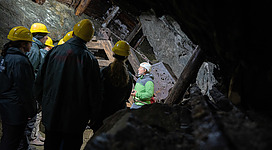 Eine Gruppe von Menschen mit Schutzhelmen steht in einer Höhle. Im Vordergrund erklärt jemand etwas zu den anderen.