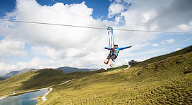 Ein Abenteuer beim Ziplining über eine grüne Landschaft. Im Hintergrund sind Berge und ein klarer Himmel zu sehen.