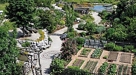 Erlebnis-Kräutergarten in Kirchberg bei Mattighofen: Ein malerischer Garten mit Kieswegen, Teichen, Holzbrücken und einer Vielzahl an Pflanzen. Verschiedene Statuen und Dekorationselemente verleihen dem Ort einen rustikalen und naturnahen Charakter.