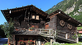 Ein traditionelles Holzhaus mit rustikalem Charme und Blumenkästen. Die Umgebung ist bergig und grün.