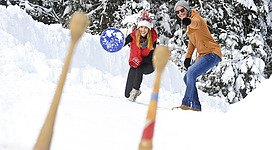 Paar beim Eisstockschießen in der verschneiten Winterlandschaft.