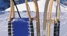 Ein Schlitten aus Holz steht auf schneebedecktem Boden in den Bergen. Die Umgebung ist klar und sonnig, mit schneebedeckten Gipfeln im Hintergrund.