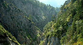 Eine beeindruckende Schlucht mit steilen Felsen und grünen Bäumen. Der Himmel ist leicht bewölkt und die Atmosphäre wirkt friedlich.