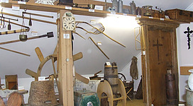 Heimatmuseum Roßbach in Roßbach: Man sieht einen Raum voller alter und traditioneller Gegenstände. Es befinden sich verschiedene Uhren, Geräte, Körbe und andere Dekorationselemente an den Wänden und auf Regalen. Der Raum hat einen nostalgischen und authentischen Charakter, der auf eine vergangene Zeit hinweist.