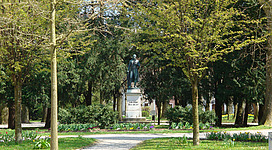 Palmpark in Braunau am Inn: In diesem Bild sehen wir einen schönen Park mit zahlreichen Bäumen und Sträuchern. In der Mitte des Parks steht eine Statue auf einem Sockel. Die Statue zeigt eine männliche Figur in historischer Kleidung. Der Park ist gut gepflegt und wirkt einladend.