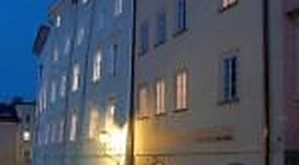 Ein nächtliches Stadtbild mit beleuchteten Fenstern in hellen Gebäuden. Die Atmosphäre ist ruhig und einladend.