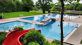 Erlebnisbad Bad Kreuzen in Bad Kreuzen: Ein idyllischer Garten mit einem großen Swimmingpool. Der Pool ist von saftigem Grün umgeben - Bäume, Sträucher und Blumen. Ein Rutsche führt in den Pool, der für Erfrischung an heißen Sommertagen einlädt.