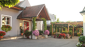 Ein einladendes Gebäude mit blühenden Pflanzen und einem schattigen Außenbereich. Die Atmosphäre ist freundlich und einladend.